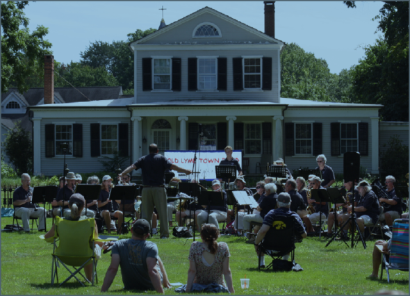 Photo of the Old Lyme Town Band playing with spectators sitting on the grass and in folding chairs.